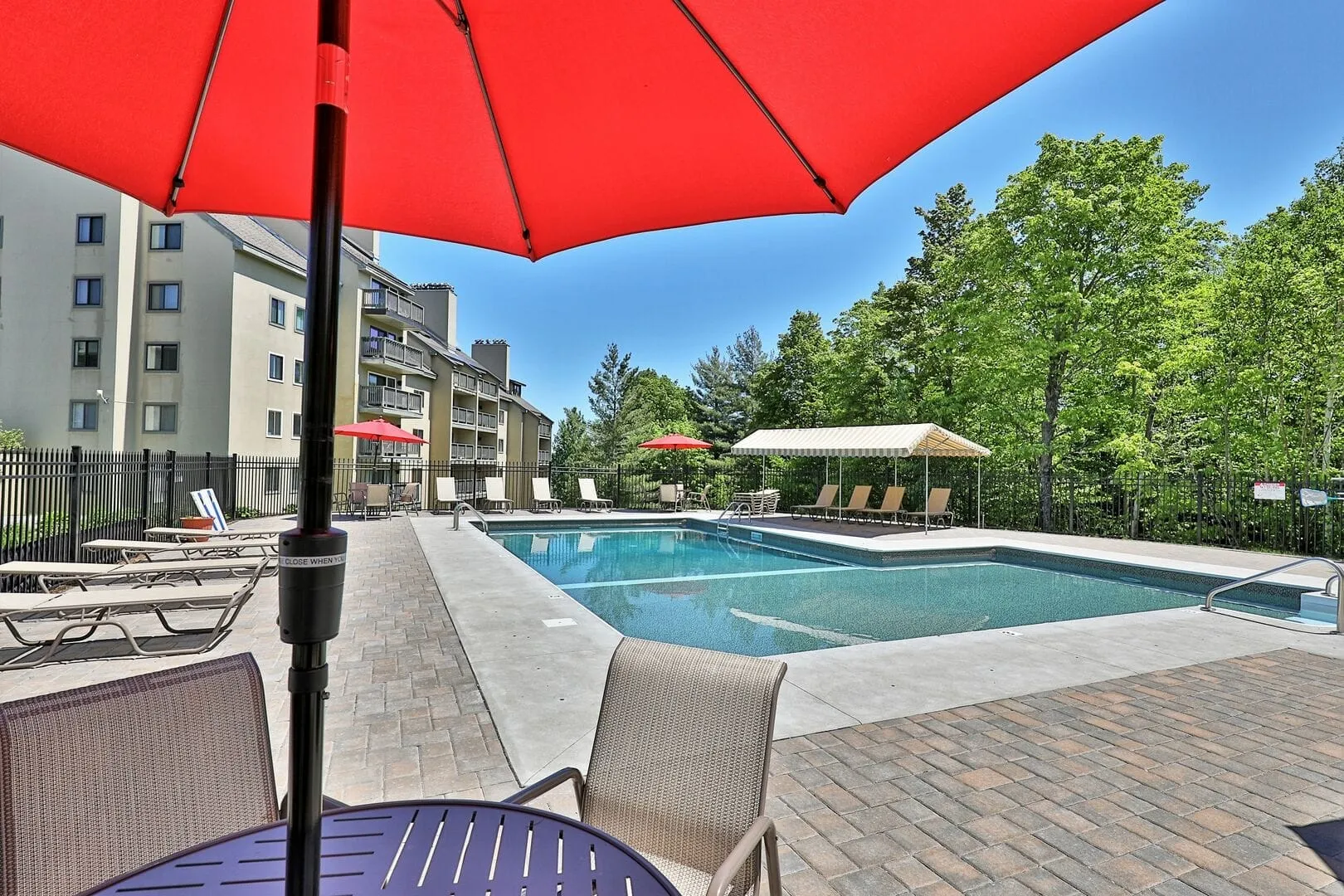 Heated outdoor swimming pool with red umbrellas, lounge chairs, and picnic tables at Mountain Green Resort vacation rentals in Killington Vermont